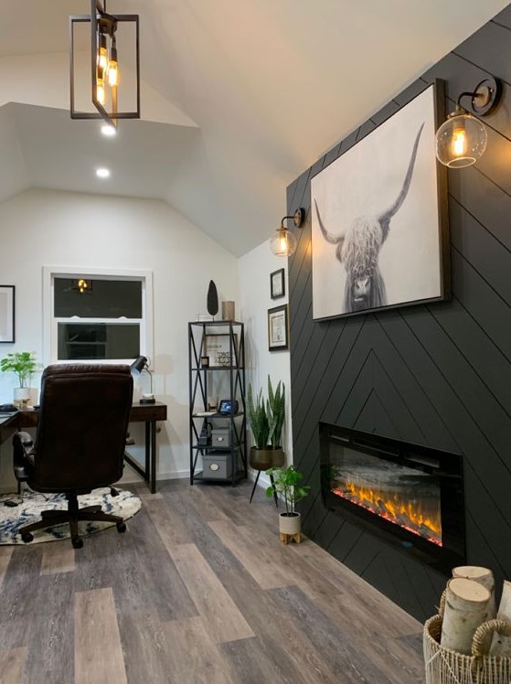 a farmhouse home office with a built-in fireplace clad with grey planked, a dark stained corner desk, a leather chair and potted plants
