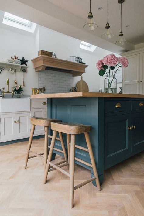 a farmhouse kitchen with creamy shaker style cabinets, a teal kitchen island with butcherblock countertops, wooden stools and a delicate hood