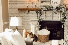 a fireplace deocrated with fresh greenery, candles and some firewood by its side for a cozy feel