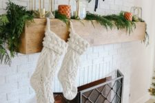 a fireplace styled with evergreens, an evergrene wreath and candle lanterns plus stockings for a cool look