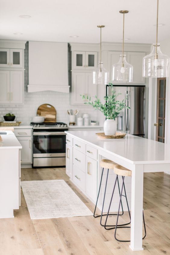 a fresh white kitchen with a farmhouse feel, with a large kitchen island with storage and a seating zone and glass pendant lamps