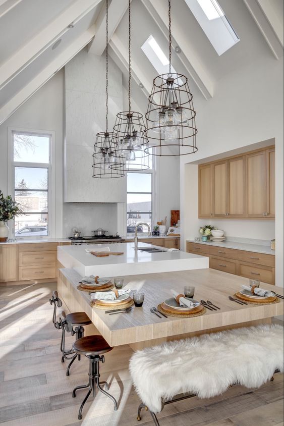 a light-filled Scandinavian kitchen with light-stained cabinets, a large white hood, a white kitchen island with an additional table attached