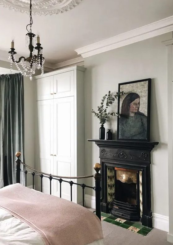a lovely bedroom with Georgian touches, a crystal chandelier, a vintage fireplace, a forged bed and greenery