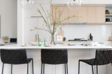 a lovely contemporary kitchen with white and stained cabinets, a white kitchen island, black woven stools, pendant lamps