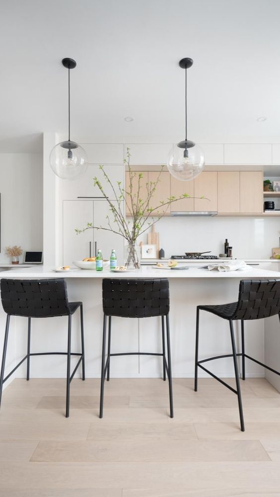 a lovely contemporary kitchen with white and stained cabinets, a white kitchen island, black woven stools, pendant lamps