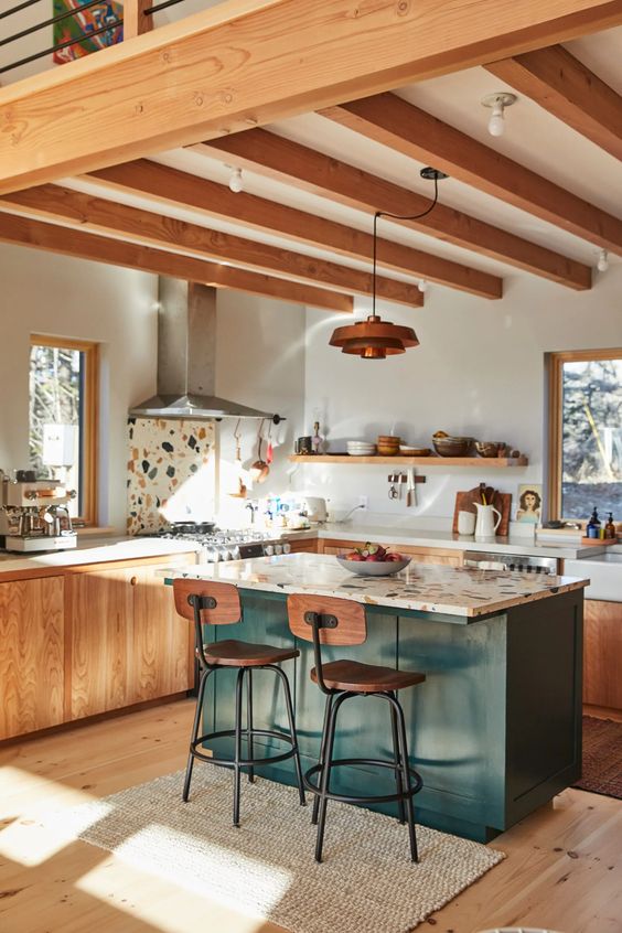 a lovely mid-century modern kitchen with stained lower cabinets, wooden beams on the ceiling, a dark green kitchen island and terrazzo surfaces