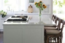 a lovely modern white kitchen with shaker cabints, stained chairs, glass pendant lamps and a white marble tile backsplash