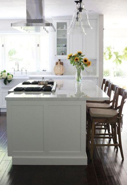 a lovely modern white kitchen with shaker cabints, stained chairs, glass pendant lamps and a white marble tile backsplash