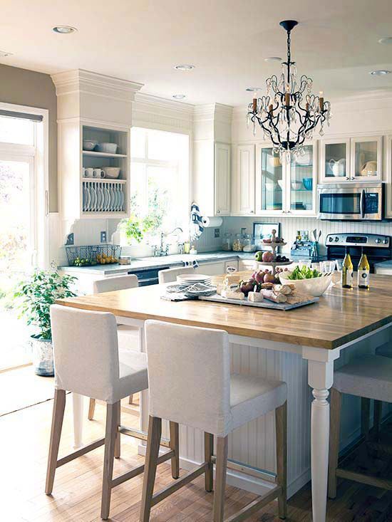 a lvoely kitchen with vintage touches, with shaker and planked cabinets, a large kitchen island with elegant white stools and a crystal chandelier