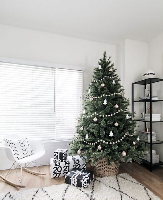 a minimalist Scandi Christmas tree decorated with white and silver ornaments, white pompom garlands and a basket plus black and white gift boxes