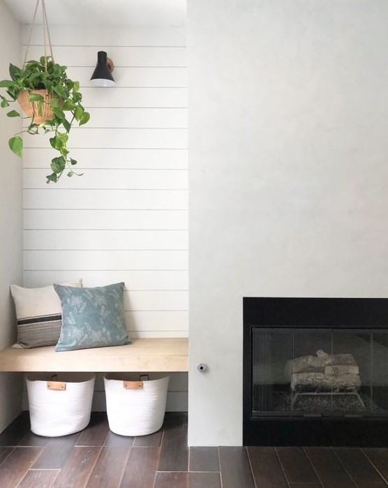 a minimalist farmhouse space with a built-in fireplace, a built-in seat wiht pillows and baskets under it is a lovely nook