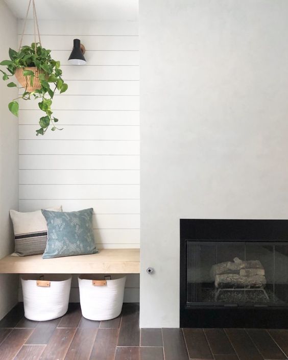 a minimalist farmhouse space with a built in fireplace, a built in seat wiht pillows and baskets under it is a lovely nook