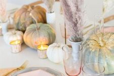 a modenr pastel Thanksgiving tablescape with pastel and gidled pumpkins, pastel pampas grass, pastel plates and gold cutlery