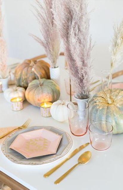 a modenr pastel Thanksgiving tablescape with pastel and gidled pumpkins, pastel pampas grass, pastel plates and gold cutlery