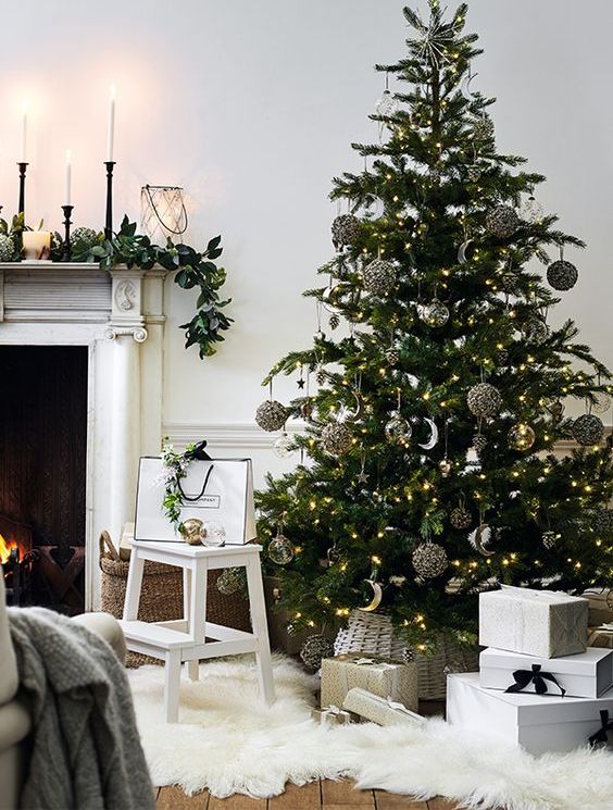 a modern Christmas tree decorated with black sequin, gold and silver half moon ornaments plus a neutral basket tree skirt