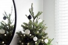 a modern Christmas tree decorated with blak and white ornaments and pompom lights plus an old sweater as a tree skirt