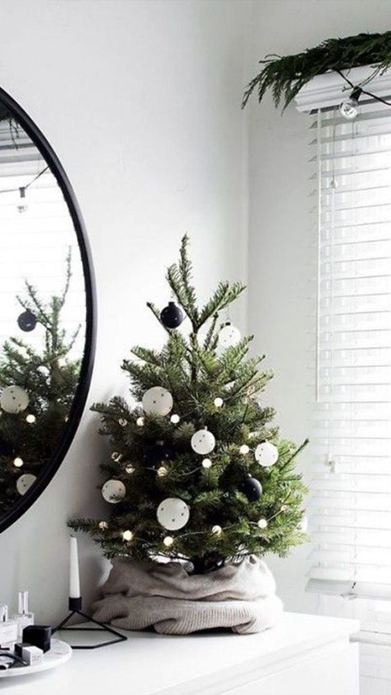 a modern Christmas tree decorated with blak and white ornaments and pompom lights plus an old sweater as a tree skirt