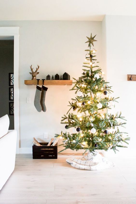 a modern Christmas tree with black and white ornaments, with lights and a gold star topper plus a windowpane tree skirt