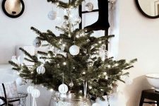 a modern Scandinavian Christmas tree with white ornaments, lights and a silver metallic tree skirt is a stylish idea