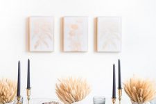 a modern Thanksgiving tablescape with a black runner, plates and tall candles, wheat arrangements and grey glasses