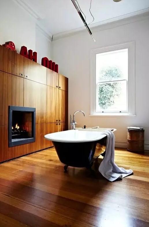 a modern bathroom with a wooden floor, a wooden storage unit that includes a fireplace, monograms and a black vintage bathtub