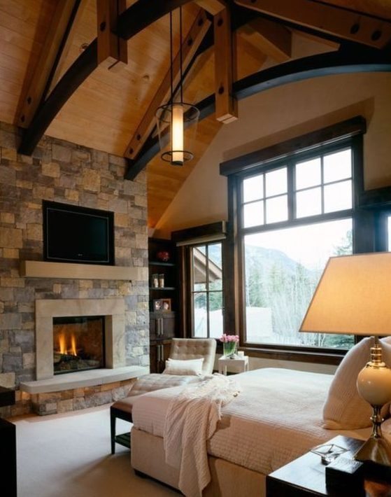 a modern chalet bedroom with a stoen clad fireplace, comfy refined furniture and touches of black for some drama