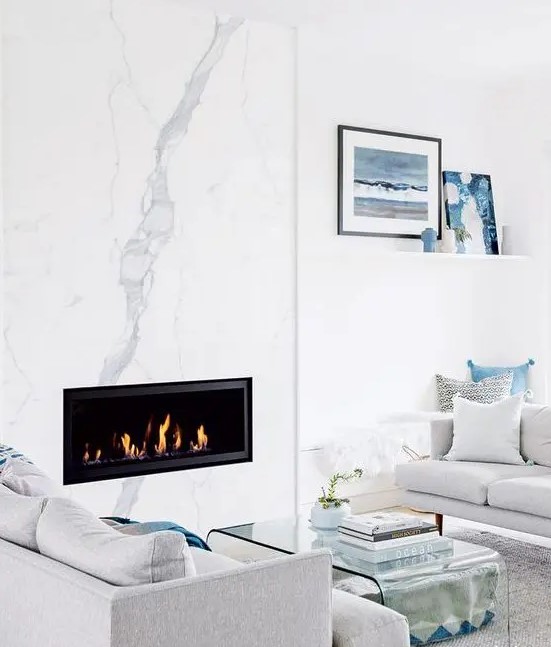 a modern coastal living room with a white marble fireplace, neutral furniture and blue accents for a beachy feel