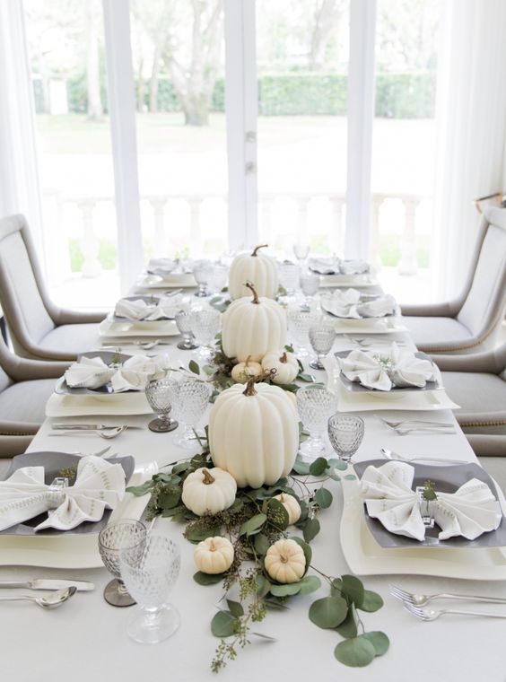 a modern elegant Thanksgiving tablescape with a greenery runner, white pumpkins, grey plates and glasses is very chic