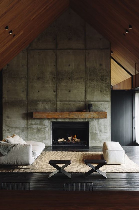 a modern industrial living room with an oversized concrete fireplace and a rough wooden mantel plus comfy furniture