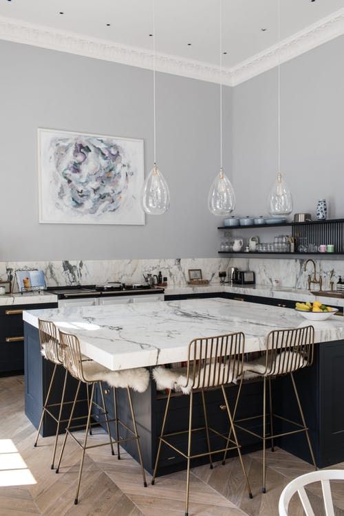 a modern kitchen with navy lower cabinets, a white marble backsplash and countertops, a large kitchen island with brass metal stools