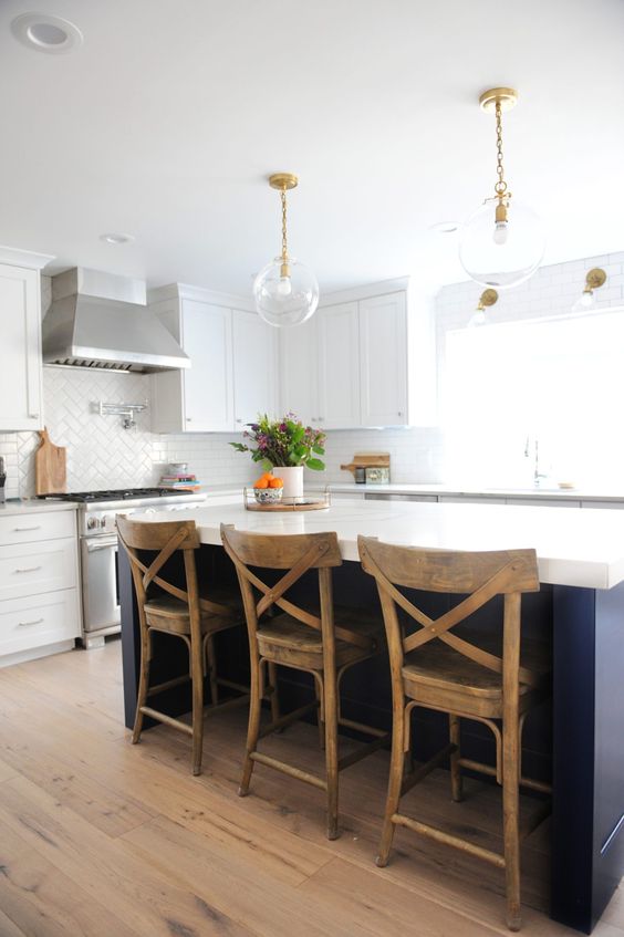 a modern kitchen with white shaker style cabinets, a navy kitchen island with stained stools and pendant lamps on chain