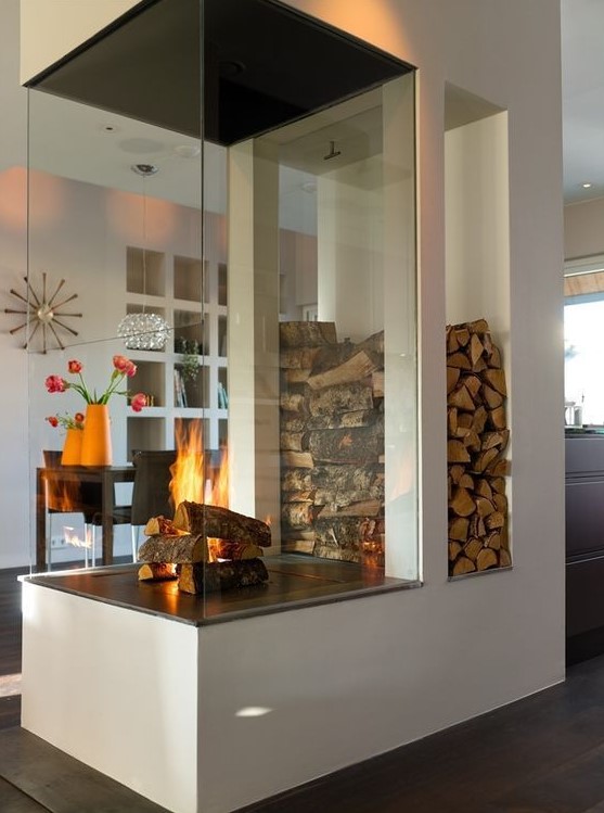a modern white fireplace with a glass cover and firewood storage is a nice space divider and is a very cozying up piece
