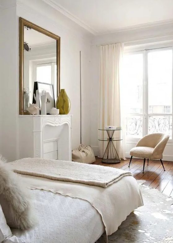 a neutral Parisian bedroom with a non-working fireplace, neutral furniture and linens and pretty artworks