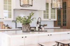 a pretty modern farmhouse kitchen done in creamy shades, with a white marble backsplash and a ahood, a large kitchen island and neutral stools