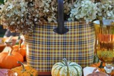 a pretty rustic Thanksgiving tablescape with woven placemats, plaid plates and a basket with dried hydrangeas, pumpkins and amber glasses