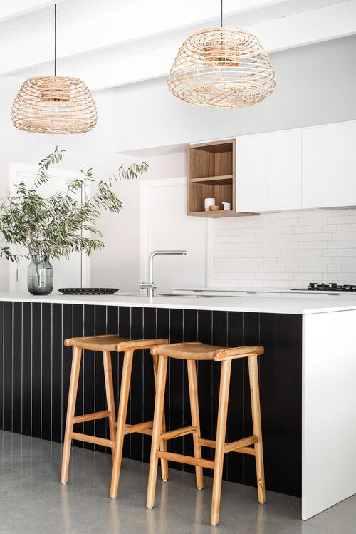 a refined contrasting kitchen with sleek white cabinets, a white subway tile backsplash, a large kitchen island with black planks, woven pendant lamps