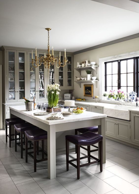 a refined vintage dove grey kitchen with shaker style cabinets, a vintage chandelier, a large kitchen island with purple stools
