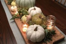 a rustic Thanksgiving centerpiece of a cutting board with heirloom pumpkins, greenery, candles