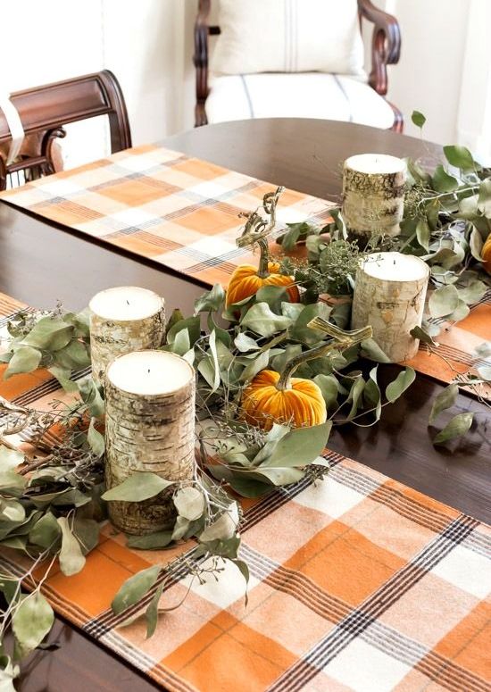 a rustic fall or Thanksgiving tablescape with bright plaid runners, greenery, orange velvet pumpkins and wooden candleholders is cool
