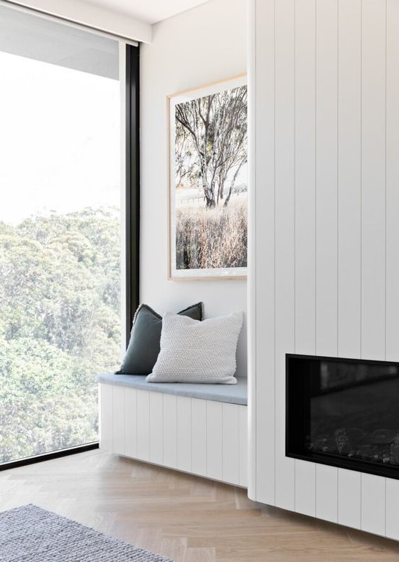 a serene nook with a wood clad built-in fireplace, a built-in bench with pillows and a lovely view plus a chic artwork