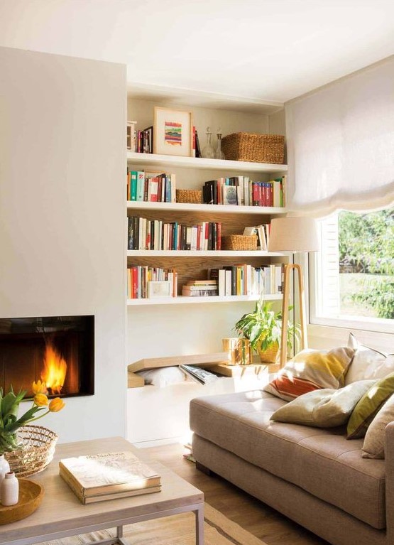 a sleek built-in fireplace, a bench and built-in shelves, a tan couhc with pillows form a cozy and welcoming reading nook