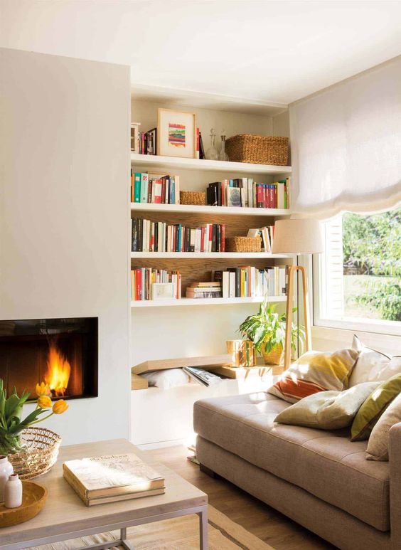 a sleek built-in fireplace, a bench and built-in shelves, a tan couhc with pillows form a cozy and welcoming reading nook