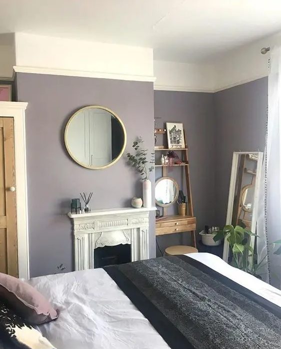 a small yet cozy bedroom with lavender walls, a refined built-in fireplace, a mini stained wood shelving unit and a round mirror