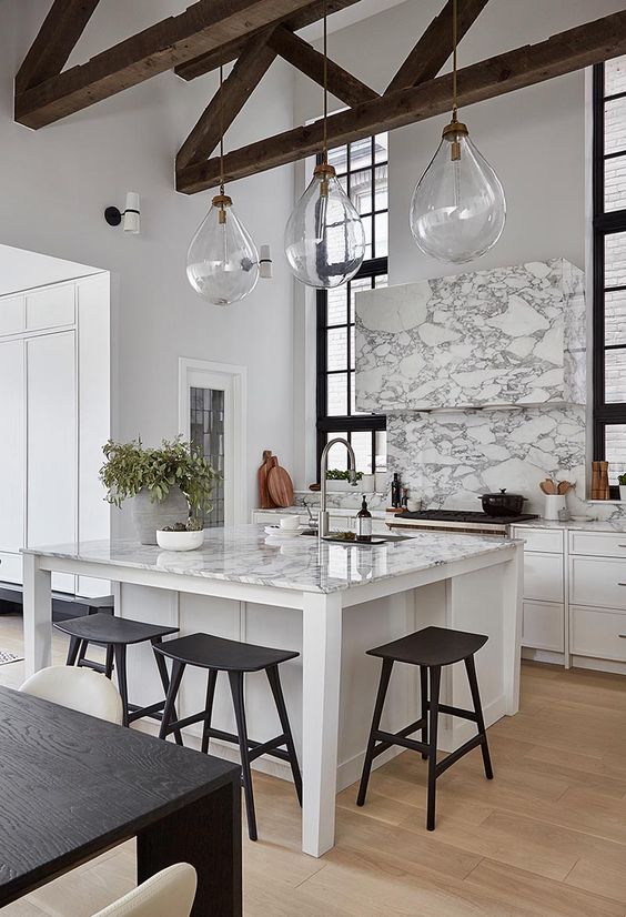 a sophisticated white kitchen with marble touches, a small kitchen island with a seating zone and black stools here