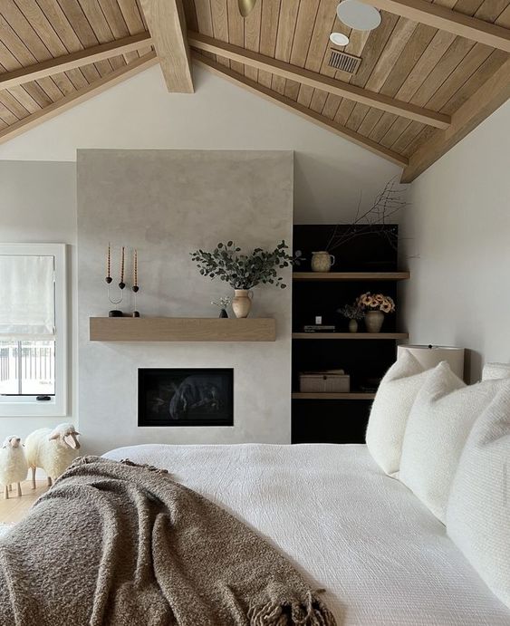 a stylish neutral bedroom with a built-in fireplace, built-in shelves, a bed with neutral bedding, sheep for decor
