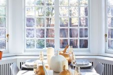 a very laconic modern tablescape with a paper table runner, pumpkins and pillar candles will be perfect for a Thanksgiving party