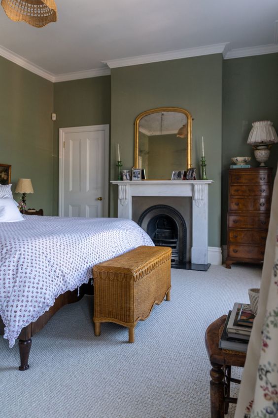 a vintage bedroom with green walls, a fireplace, a bed with printed bedding, a woven bench, stained furniture