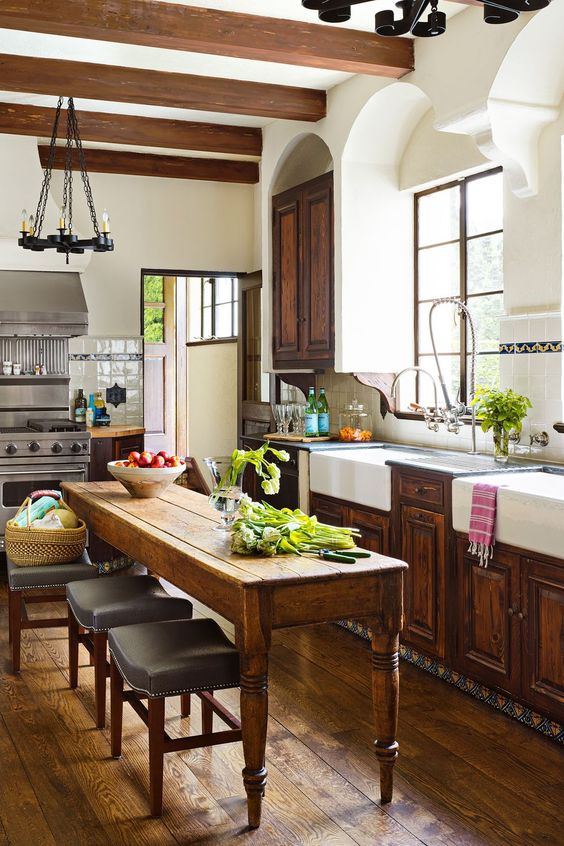 a vintage rustic kitchen with refined dark stained cabinets, a long table that doubles as a kitchen island and vintage chandeliers