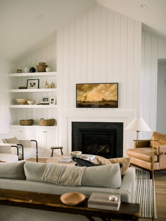 a welcoming farmhouse living room with a built-in fireplace, a grey sofa, a leather chair, built-in shelves and a cabinet