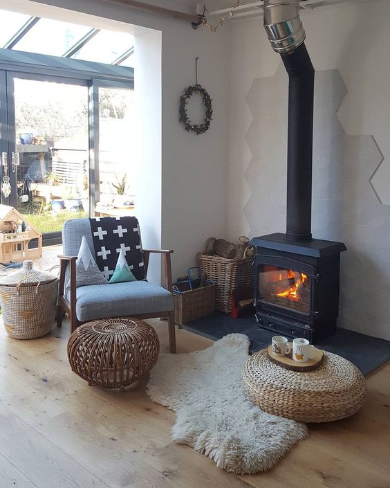 a welcoming modern space with a black hearth, a chair, a rattan table and a jute ottoman and some baskets for firewood